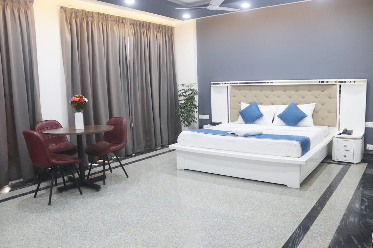 Ein Hotelzimmer mit Bett, Nachttisch, Stuhl, einem kleinen Tisch mit Blumenvase und Vorhängen.