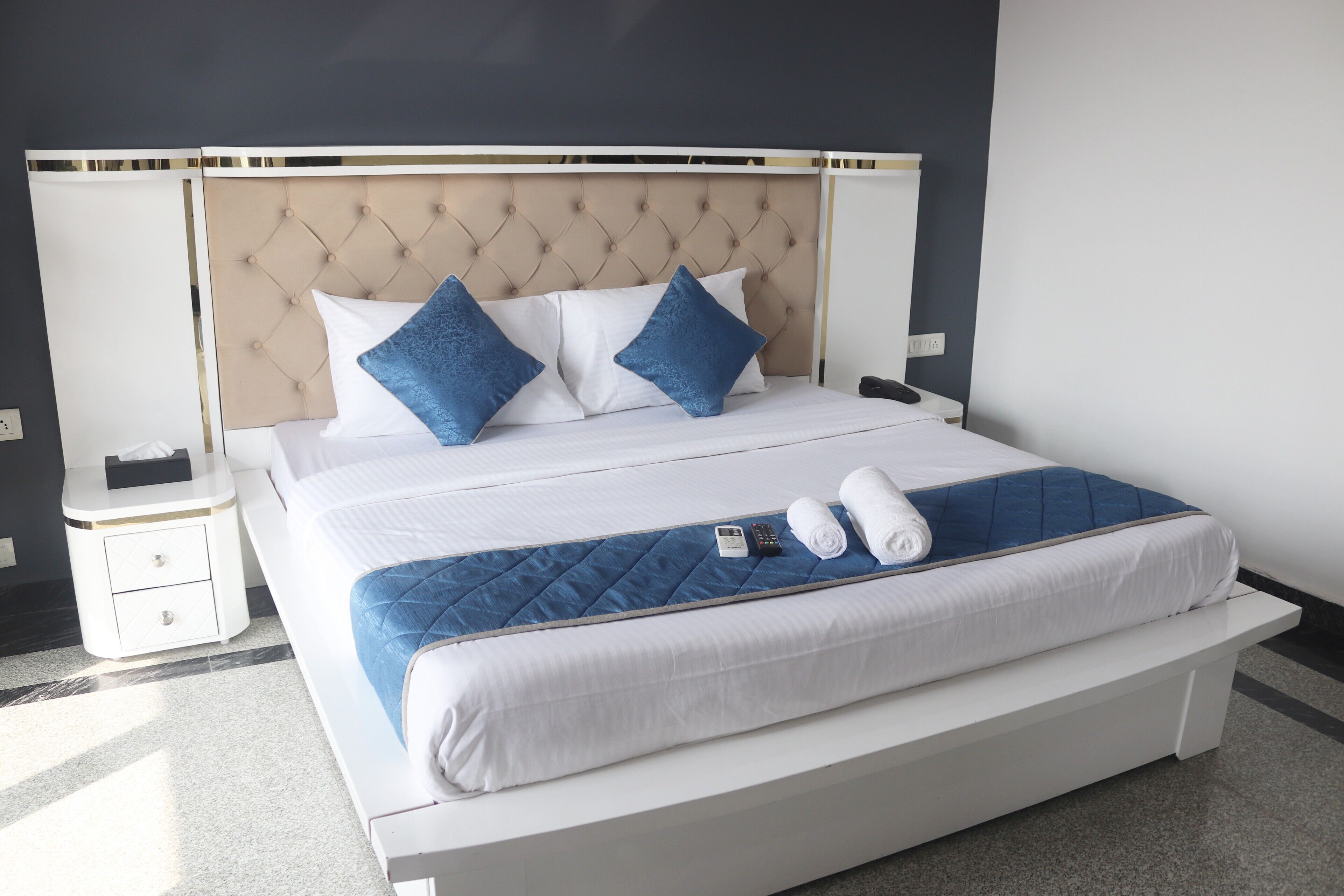 A neatly made bed with a tufted headboard, white bedding, and two blue pillows.