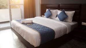 A neatly made bed with a quilted blue and white bedspread, two pillows, and a remote control on it. - Axon Stays Near Artemis Hospital Gurgaon Sector 52 (Gurugram)