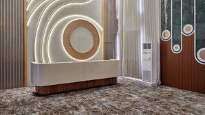 A modern reception area with a circular light feature, a wooden reception desk, and a patterned carpet. - Pride Elite Gandhinagar (Gandhinagar)