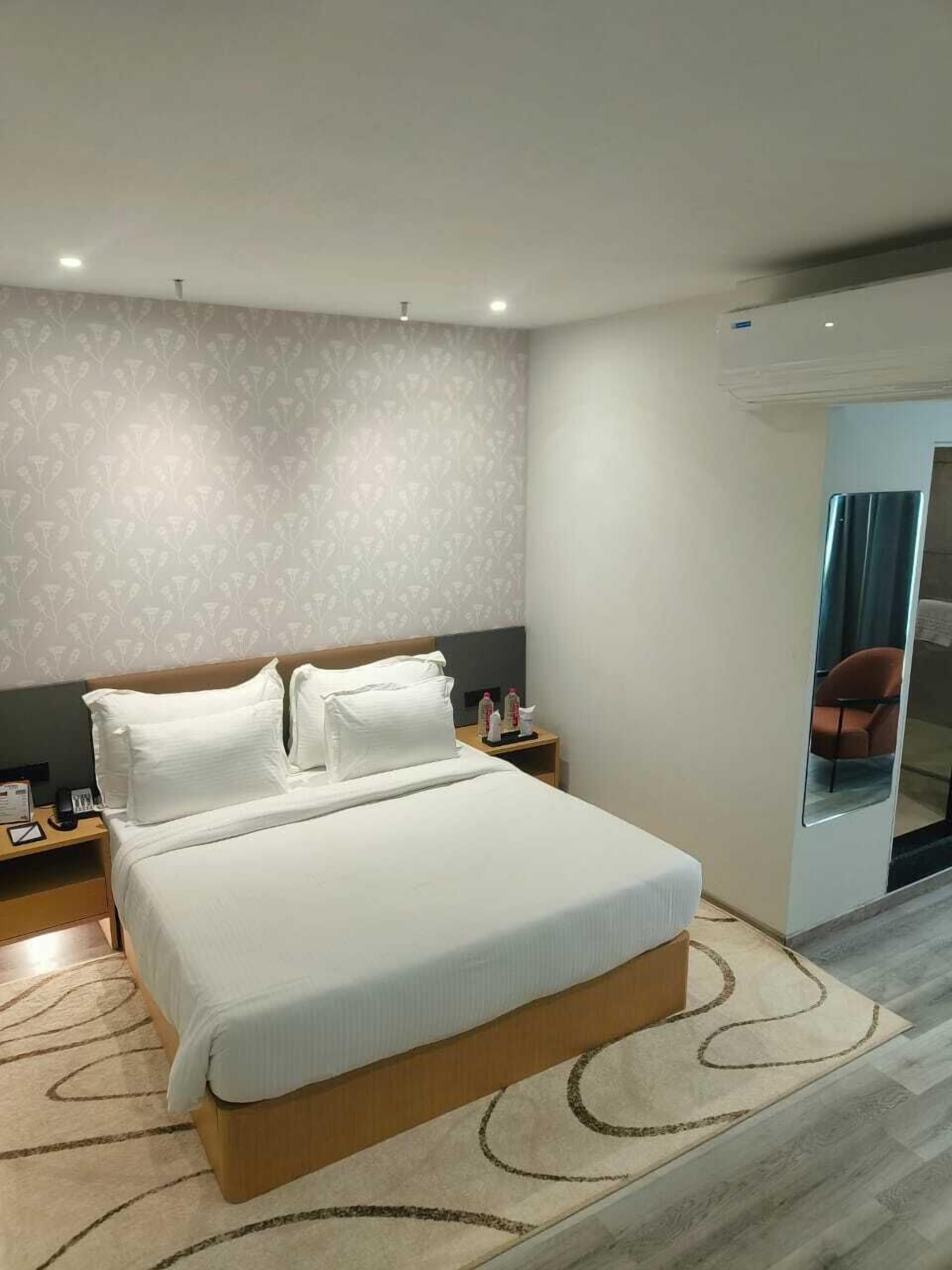 Ein modernes Hotelzimmer mit einem großen Bett, einem Nachttisch, einem Spiegel und Blick auf die Stadt durch eine Glastür.