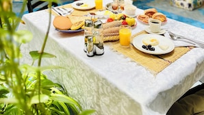A breakfast table set with various foods and drinks, surrounded by potted plants and a cozy seating area with cushions. - Riad Dar Meziana  (Chefchaouen)