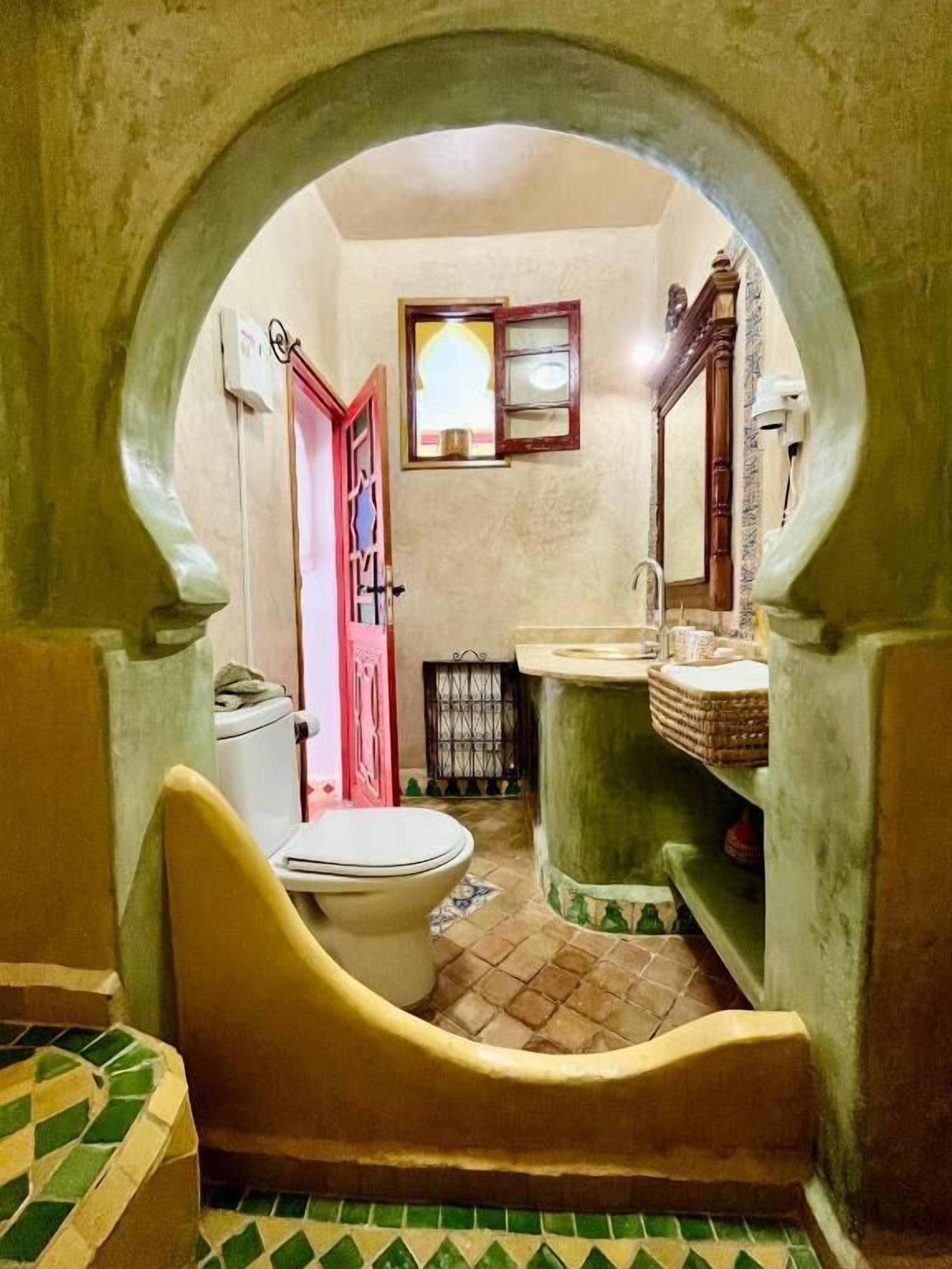 A narrow hallway leading to a bathroom with a toilet, sink, and a mirror.