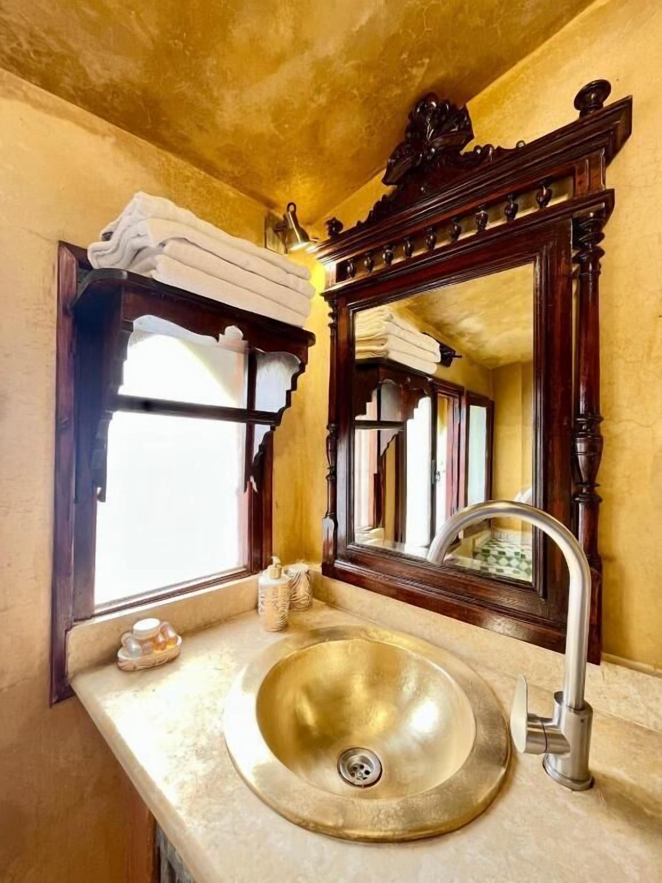 Ein Badezimmer mit einem goldfarbenen Waschbecken, einem Spiegel und einem Fenster mit Blick nach draußen.