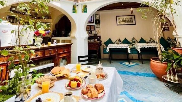 A courtyard with a dining table set for breakfast, surrounded by arches and potted plants. - Riad Dar Meziana  (Chefchaouen)