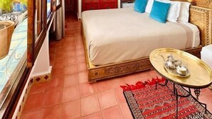 A bedroom with a large bed, a small table, and a view of the street. - Riad Dar Meziana  (Chefchaouen)