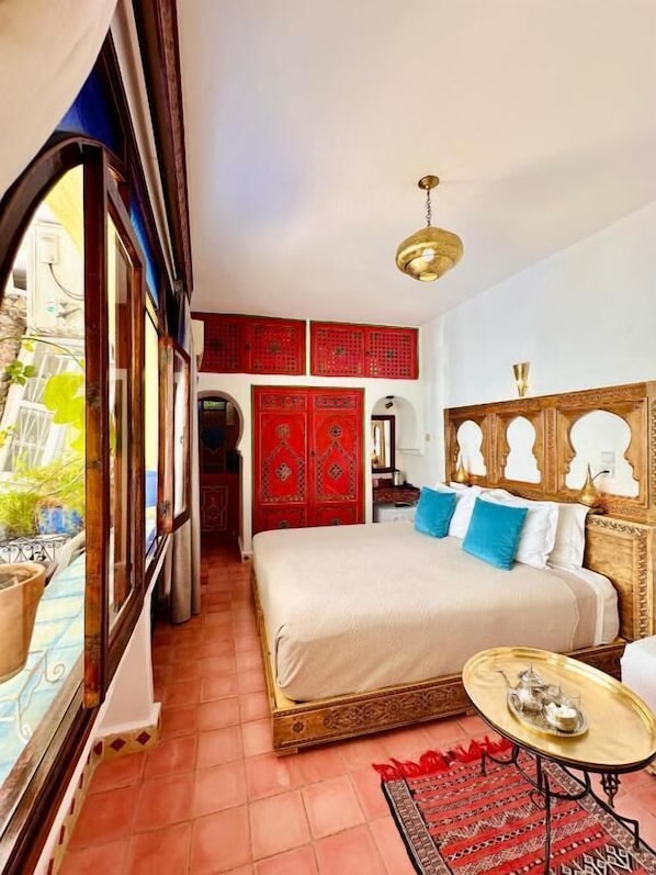 Un dormitorio con una cama grande, una mesita y vistas a la calle.