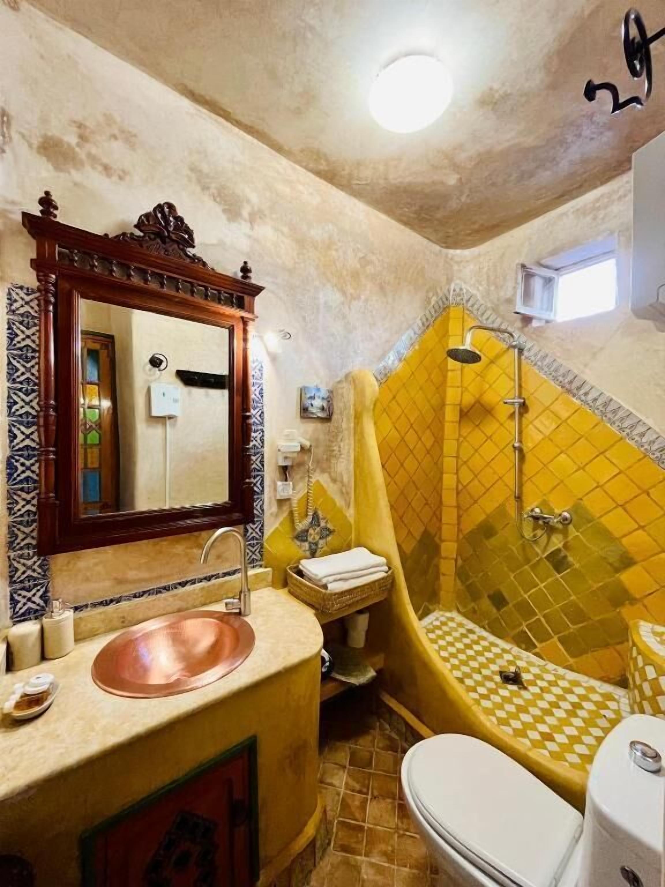 Un baño con lavabo, espejo, inodoro y una bañera amarilla.