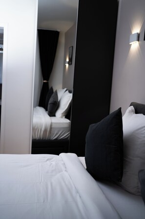 A modern hotel room with a neatly made bed, a large mirror, and a wall-mounted light fixture. - Hôtel Sofiane (Paris)