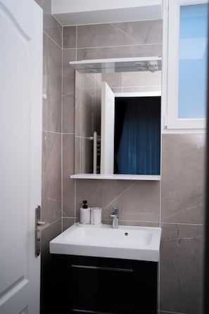 A bathroom with a white sink, a mirror above it, and a towel rack. - Hôtel Sofiane (Paris)