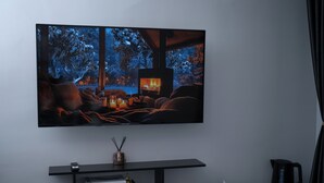 A modern living room with a large flat-screen TV mounted on the wall, a black entertainment unit below with books titled 'LONDON', 'NEW YORK', and 'PARIS', and a coffee maker on the right. - Hôtel Sofiane (Paris)