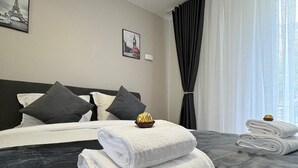 Habitación de hotel con una cama grande, ropa de cama gris oscuro, toallas blancas y dos cuadros en la pared.