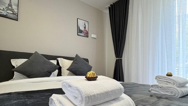 A hotel room with a large bed, dark grey bedding, white towels, and two framed pictures on the wall. - Hôtel Sofiane (Paris)