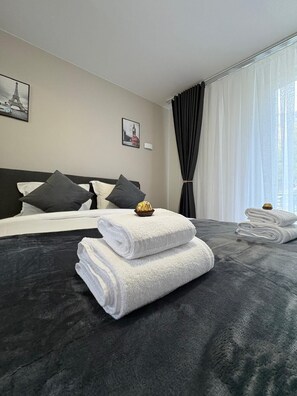 A hotel room with a large bed, dark grey bedding, white towels, and two framed pictures on the wall. - Hôtel Sofiane (Paris)