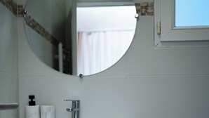 A bathroom with a round mirror, white sink, and toiletries. - Hôtel Sofiane (Paris)