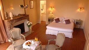 A hotel room with a large bed, two bedside tables, a fireplace, two armchairs, a small table with breakfast items, and wall sconces. - Château de Bel Air (Cérans-Foulletourte)