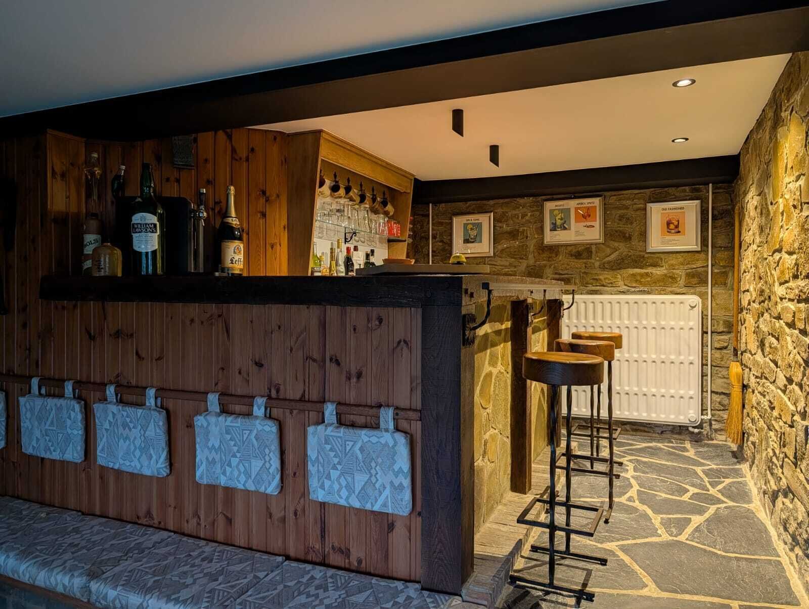 Una zona de bar con estantes de madera, taburetes y una pared de piedra.