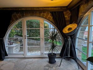 Una habitación con un arco de piedra, un amplio ventanal arqueado, una planta en maceta y una lámpara con trípode.