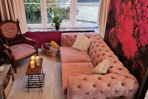 Una sala de estar acogedora con un sofá mullido, una silla de madera, una mesita con velas y vistas a zonas verdes a través de una ventana.