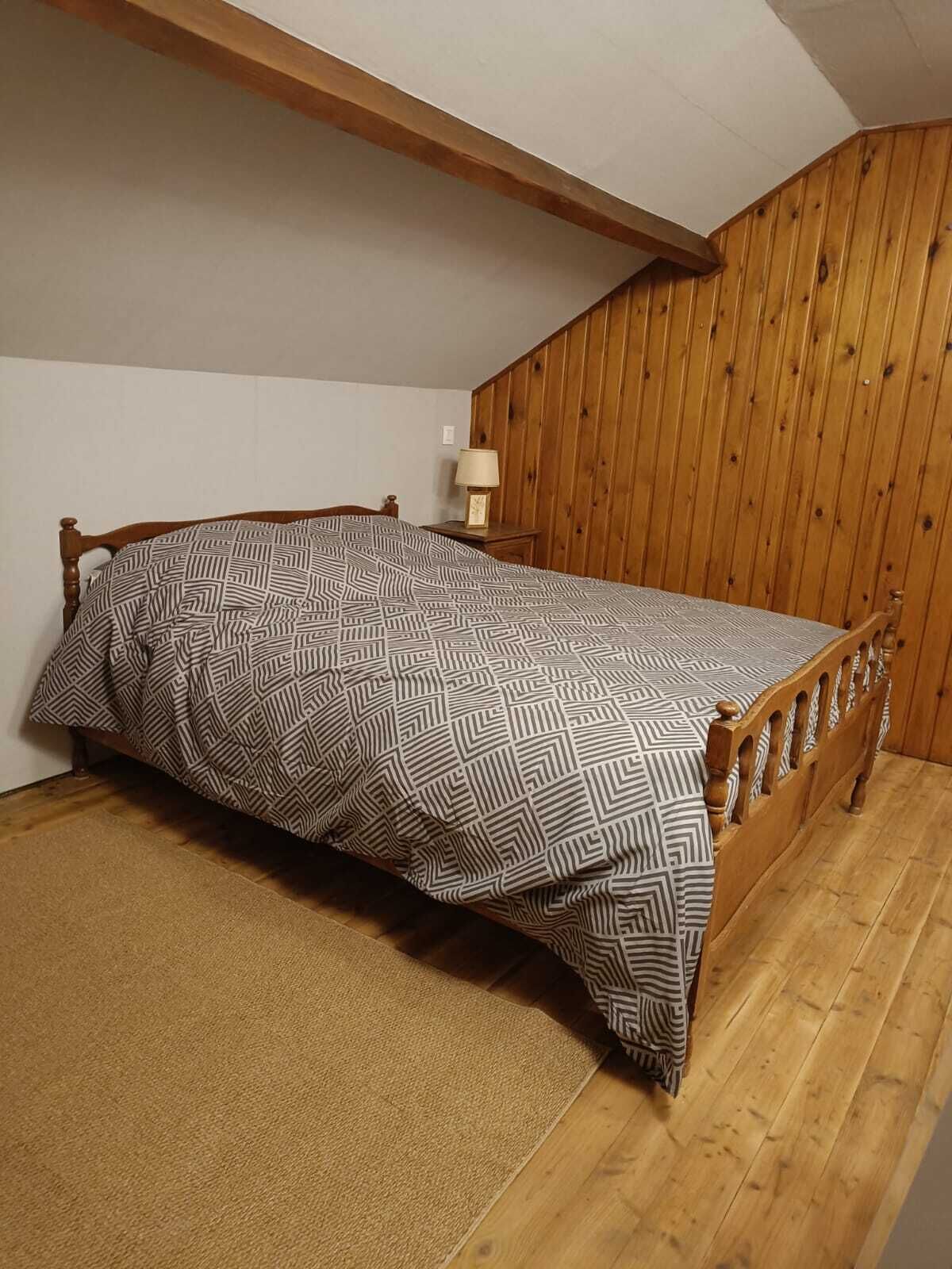 A small, cozy room with a wooden bed, a nightstand, and a lamp.