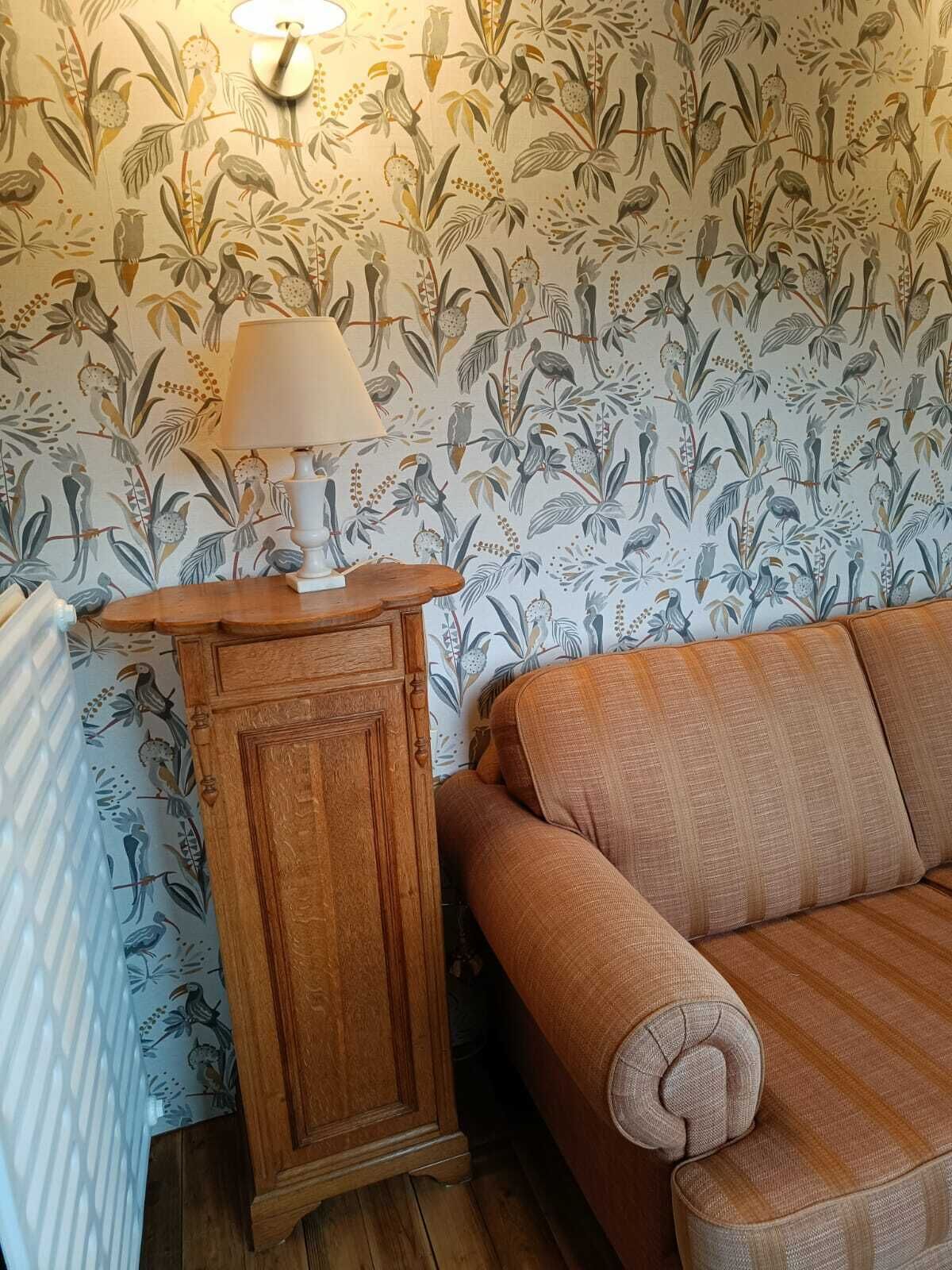 Ein Zimmer mit strukturiertem Wandpapier, einem Holzschrank, einer Lampe und einem braunen Sofa.