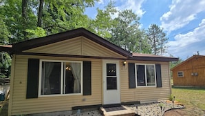 A single-story mobile home with a front porch, a small deck, and a gravel driveway. - Phenomenal 2-bedroom cabin in Saint Helen, the heart of northern Michigan. (St. Helen)
