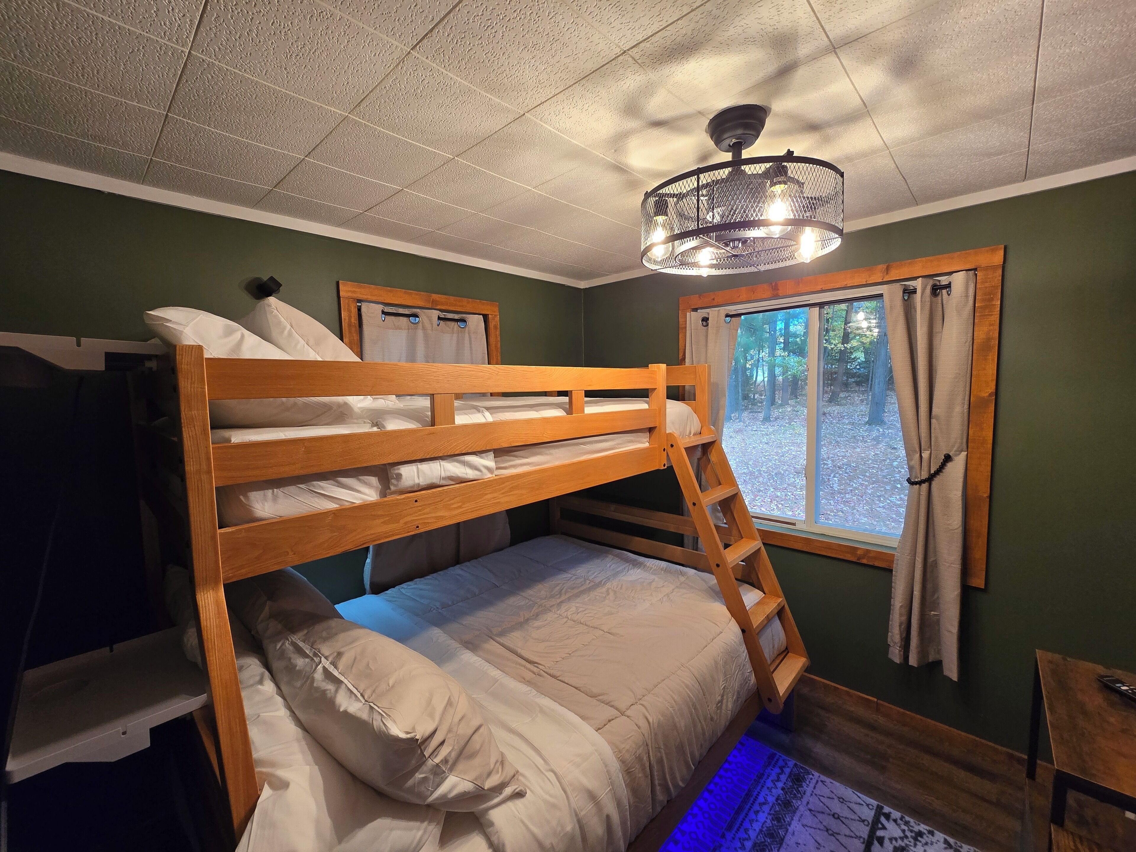 A bunk bed room with a ladder, a window with curtains, and a ceiling light fixture.