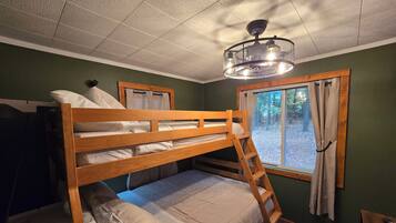 A bunk bed room with a ladder, a window with curtains, and a ceiling light fixture.
