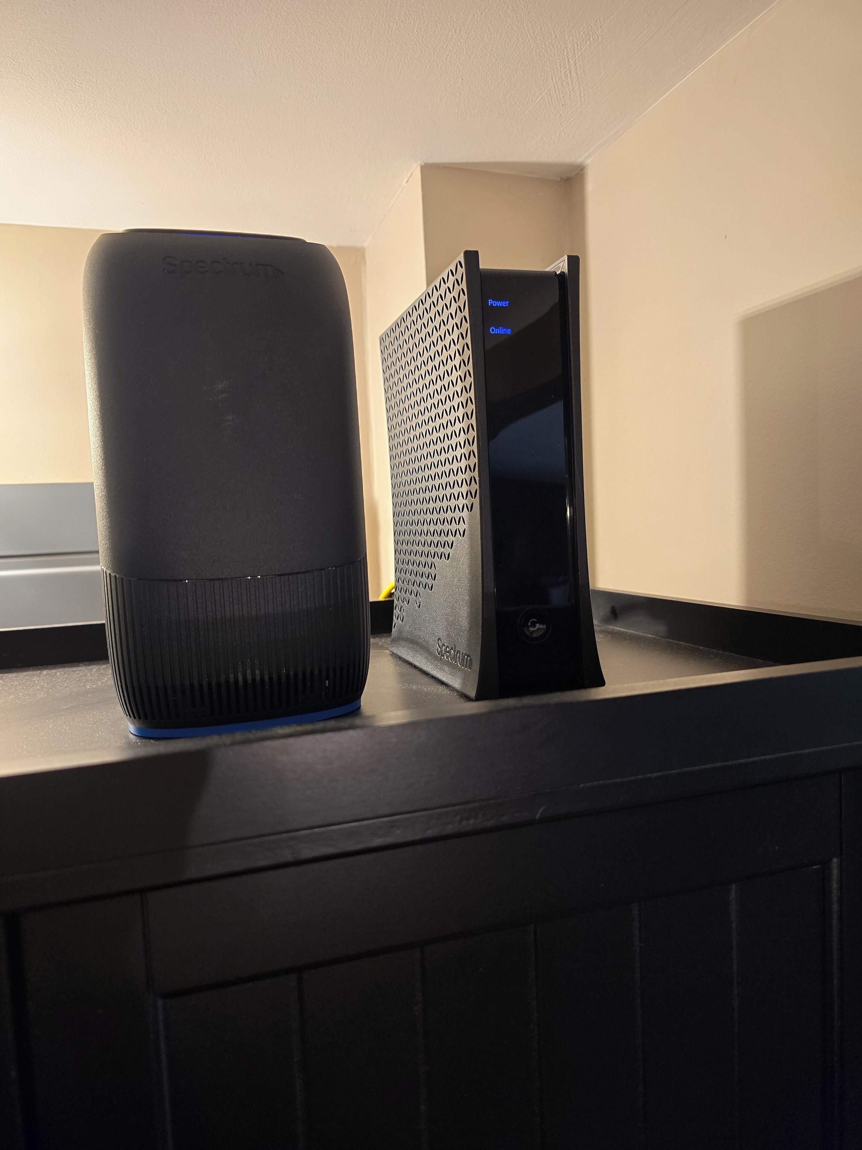 A black speaker and a black device with a mesh front on a black surface.