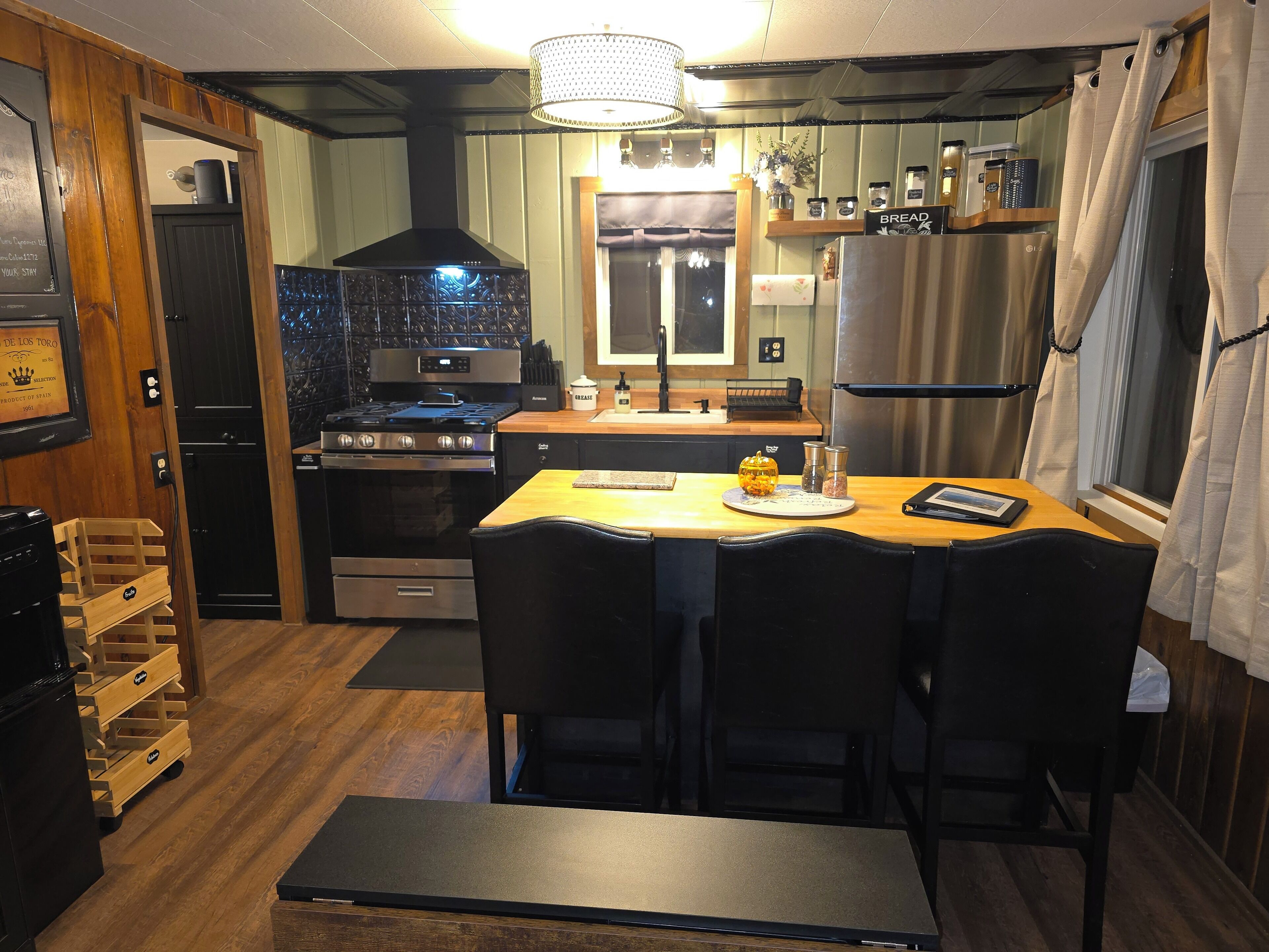 Une cuisine compacte équipée d’une cuisinière, d’un four et d’un réfrigérateur. On y trouve une table à manger avec des chaises et un banc.