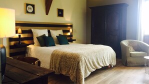 A bedroom with a large bed, bedside tables with lamps, a wooden bench, a dark wardrobe, and a chair. - LARGE BEARNAISE COUNTRY HOUSE (SAUVELADE)