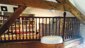 A loft-style room with exposed wooden beams, a stone wall, a green cushioned bench, a piano, and a bookshelf filled with books and games. - LARGE BEARNAISE COUNTRY HOUSE (SAUVELADE)