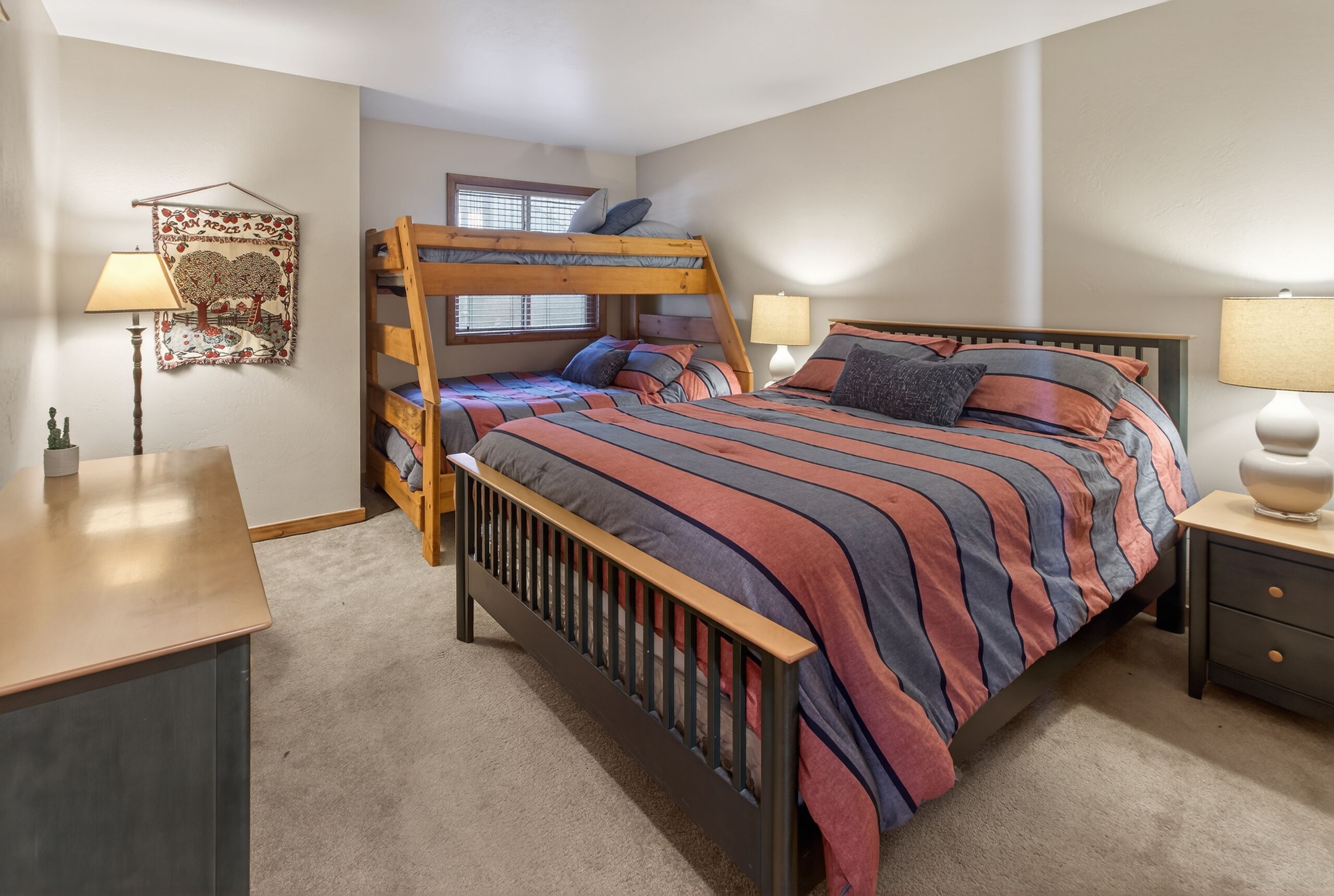 A bedroom with a bunk bed, a desk, a chair, two bedside tables with lamps, and a wall decoration.