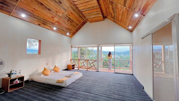 Un'ampia camera da letto con un grande letto, un soffitto in legno e un balcone con vista sul paesaggio.
