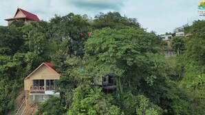 Un bungalow con tetto rosso immerso in una fitta vegetazione verde, con una scala che porta a un balcone.