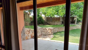 Visão pela janela de uma escadaria de pedra que leva a uma área externa com gramado e muro de pedra.