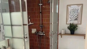 Un baño moderno con ducha de vidrio, inodoro blanco y lavamanos con espejo.