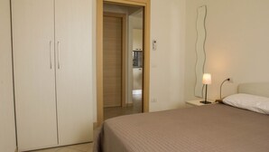 Un dormitorio con una cama, una mesita de noche con lámpara, un armario y un espejo en la pared.