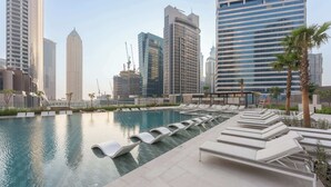 Una piscina en la azotea con sillones de descanso y vistas de edificios altos aledaños.