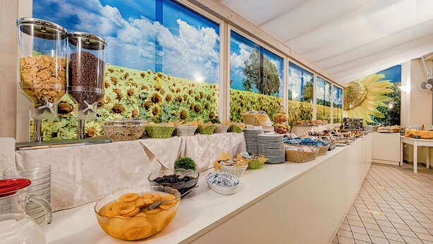 A buffet setup with various food items and a mural of a sunflower field on the wall. - Hotel Plaza Gabicce Mare (Gabicce Mare)