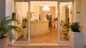 A hotel entrance with a reception desk, a chandelier, and potted plants. - Hotel Plaza Gabicce Mare (Gabicce Mare)
