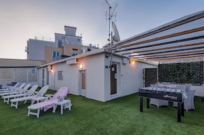 Eine Dachterrasse mit Liegestühlen, einem Kicker und einer überdachten Sitzgelegenheit.