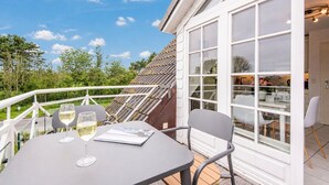 Uma varanda com mesa e cadeiras, dois copos de vinho branco e vista para o jardim e a casa.