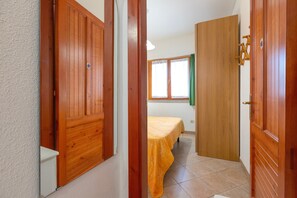 Una stanza con porte in legno, un letto con copripiumino giallo, una finestra con tenda verde e un termosifone bianco.