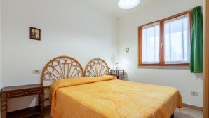 A bedroom with a bed, a nightstand, a desk, a window with curtains, and a wall-mounted picture. - Apartment 'Della Torre 40T' (isola rossa)