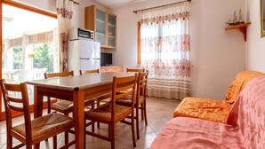 A dining area with a wooden table and chairs, a kitchen with a microwave, and a window with curtains. - Apartment 'Della Torre 40T' (isola rossa)