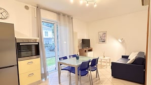 Une cuisine moderne équipée d’un réfrigérateur, d’un four et d’un coin repas avec une table en verre et des chaises bleues.