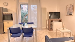 Une cuisine moderne équipée d’un four encastré, d’une table à manger avec des chaises, d’un téléviseur posé sur un meuble et d’un tableau encadré accroché au mur.