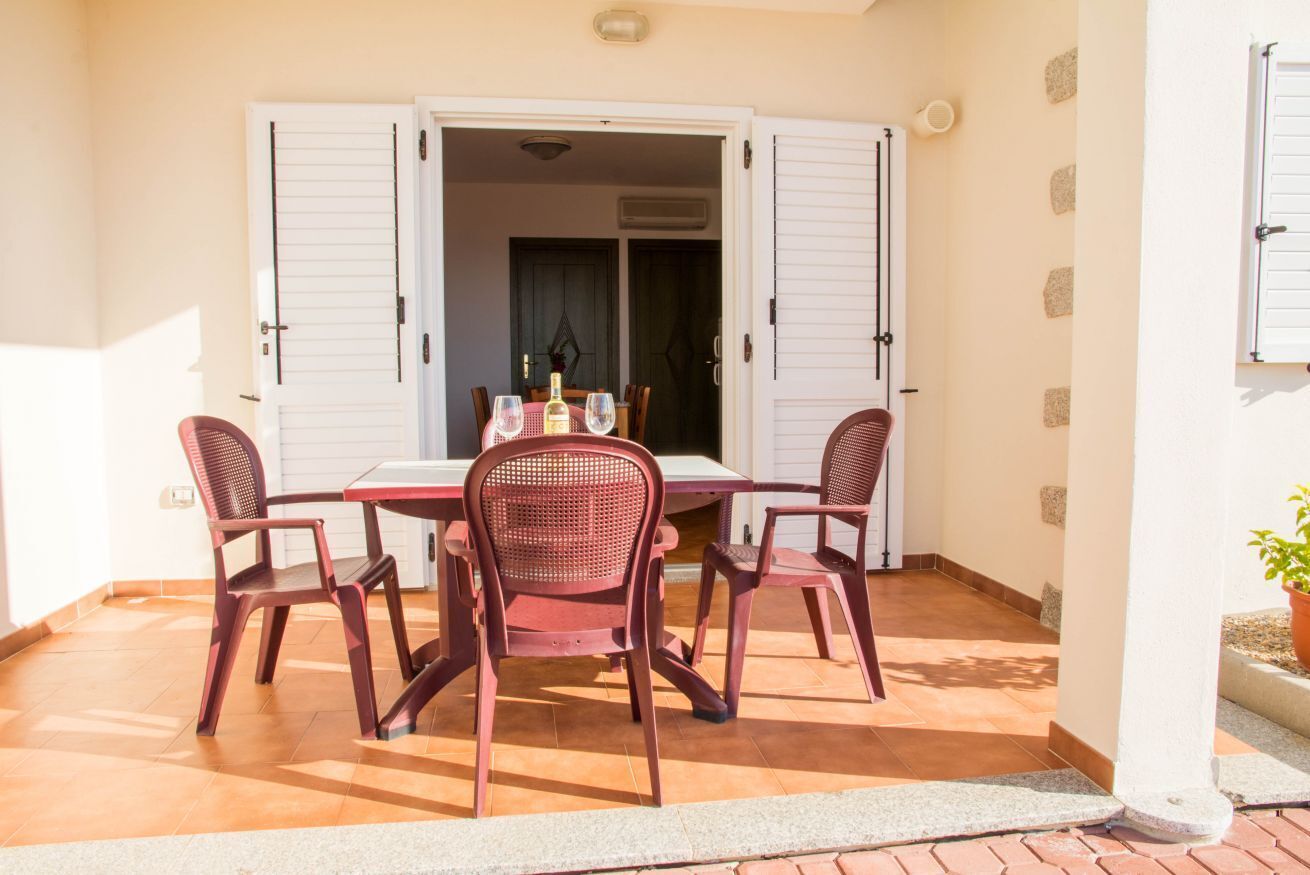 Un patio con tavolo e sedie, una porta che dà su un ambiente interno e una pianta in vaso.