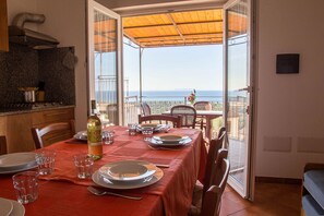 Ein Essbereich mit Tisch für vier Personen, ein Küchenbereich mit Granitarbeitsplatten und Meerblick durch einen offenen Balkon.